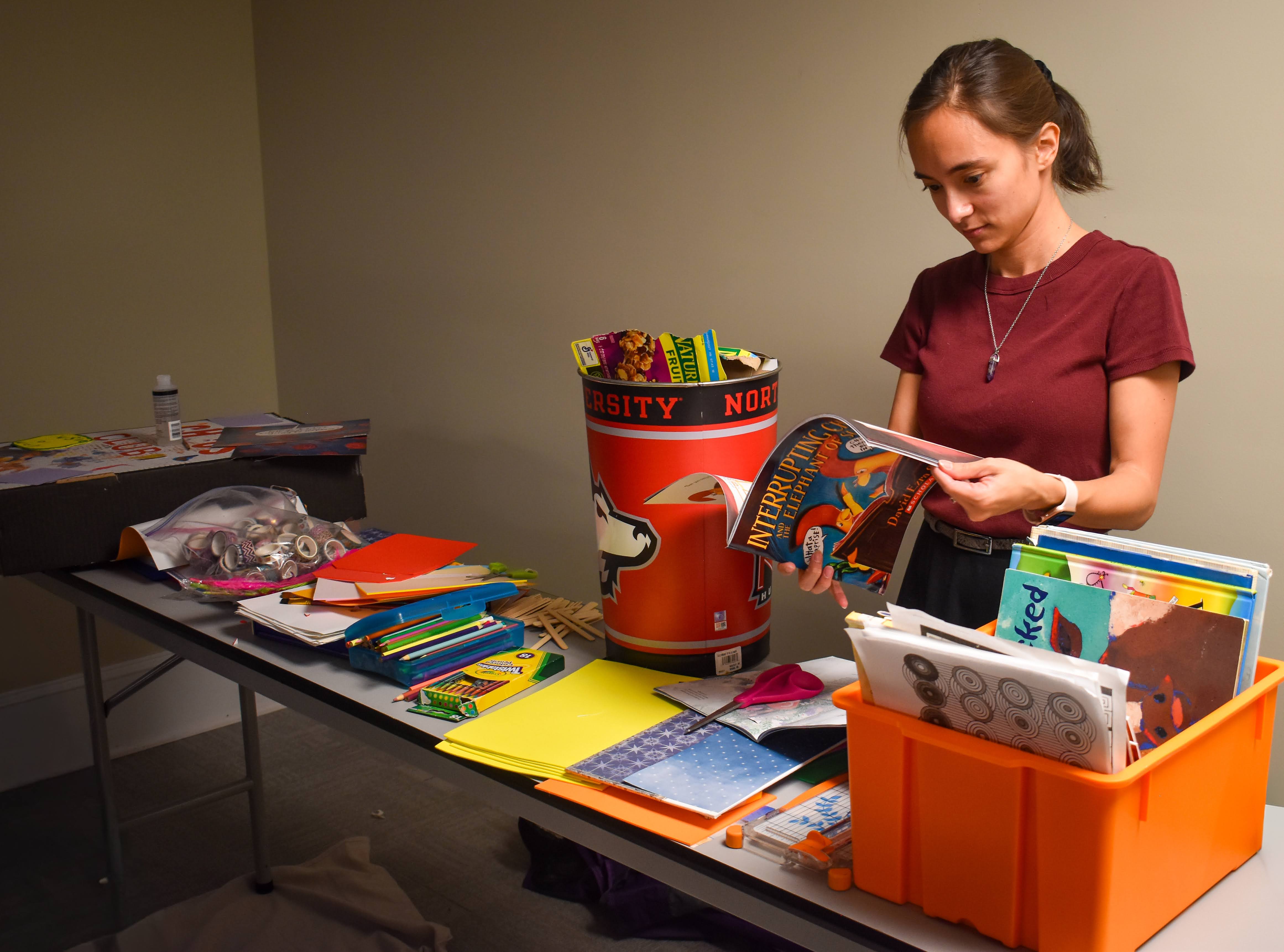 The owner of Regulated Chaos Studio, LLC, Heleena Barnett, flipping through children's books, looking for images to use for her collage at her first Chaos Club event. Other art supplies including paper, washi tape, coloring pencils, and scrapbooking materials are spread across the table. This was located at Off the Tracks Art Supply, LLC, in DeKalb, Illinois.